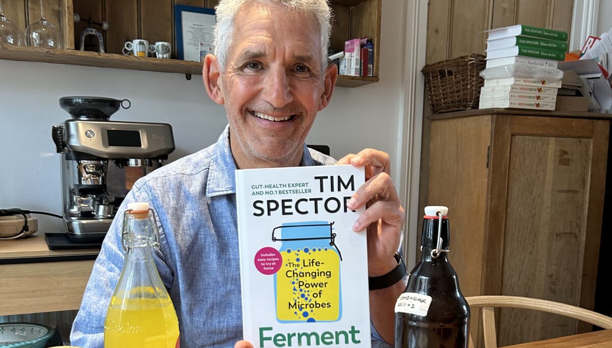 Image of Tim Spector holding new upcoming book 'Ferment', among jars and bottles of fermented food.