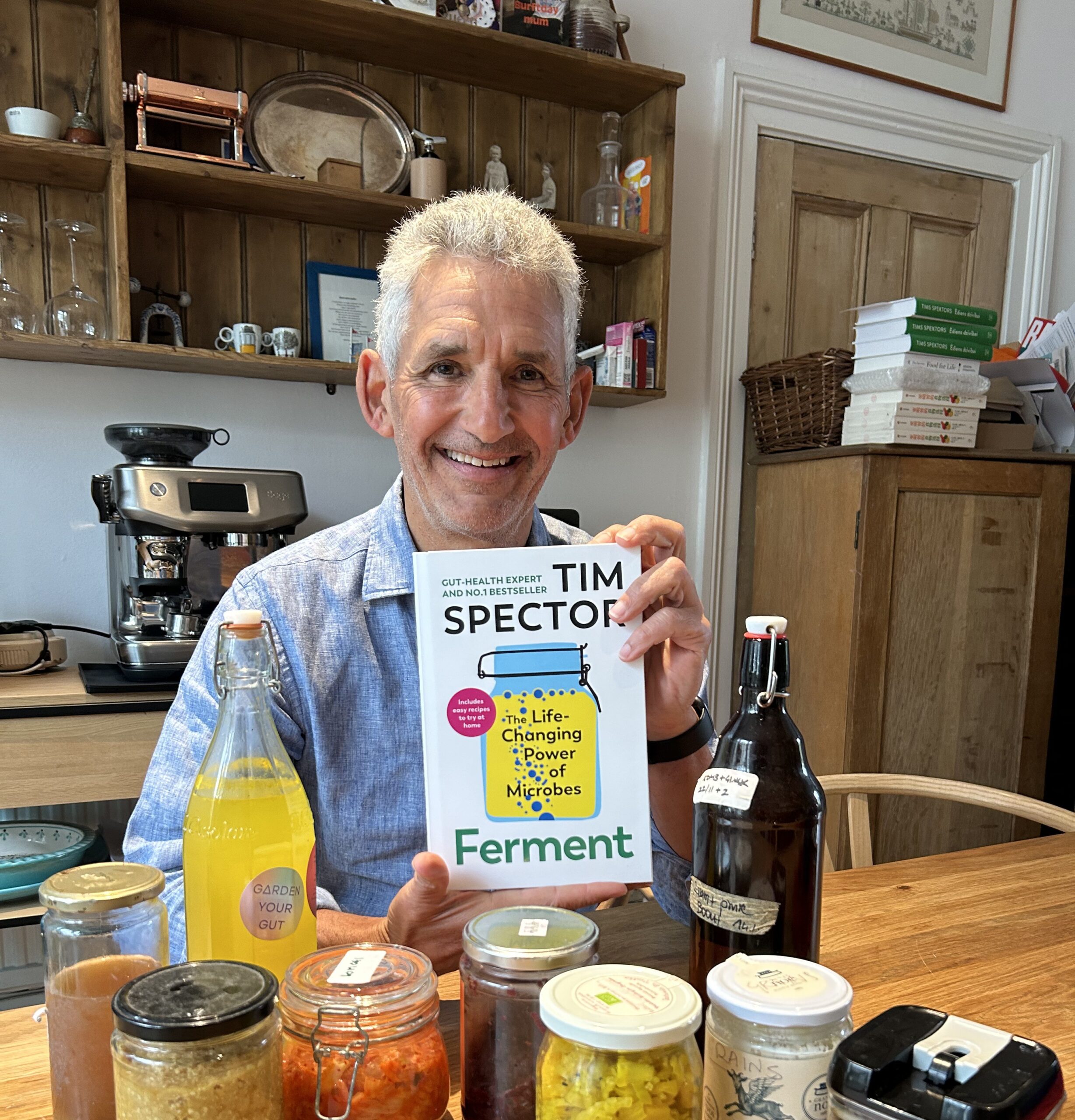 Image of Tim Spector holding new upcoming book 'Ferment', among jars and bottles of fermented food.
