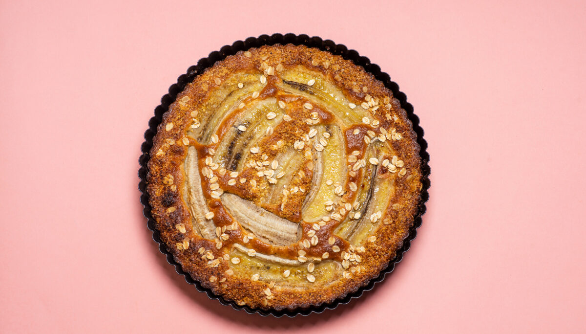 Homemade banana bread freshly baked in the pan on pink background top view