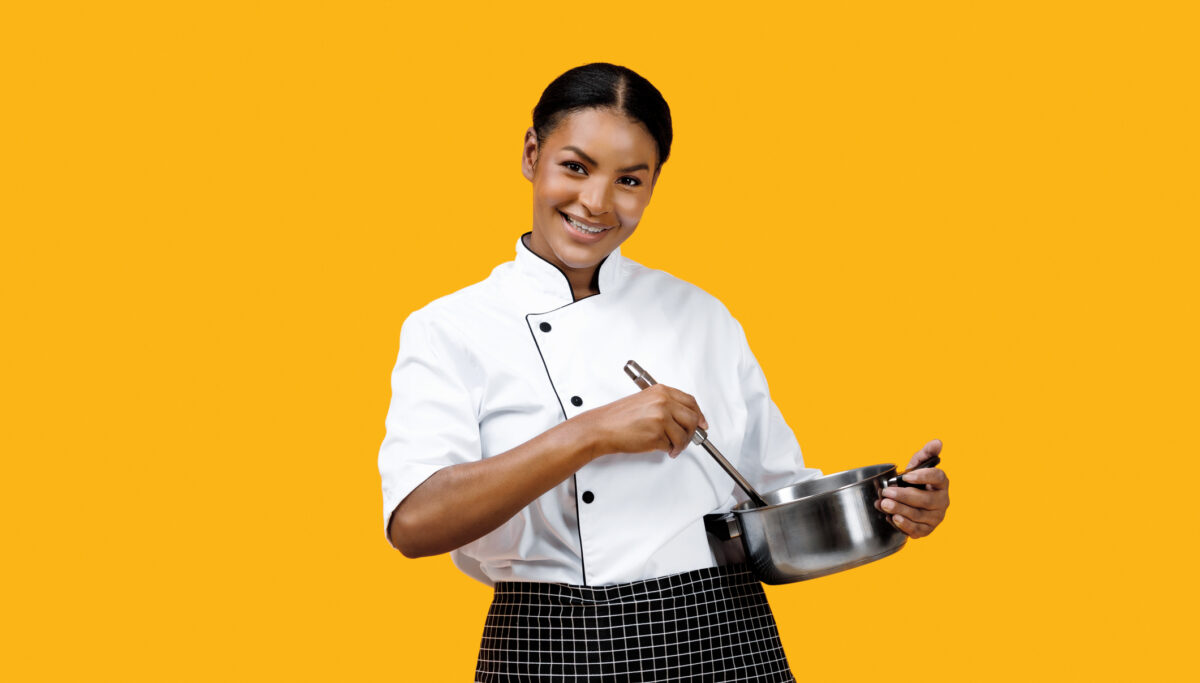 Friendly female chef stirring stainless steel pot and smiling at camera, making egg fried rice kimchi