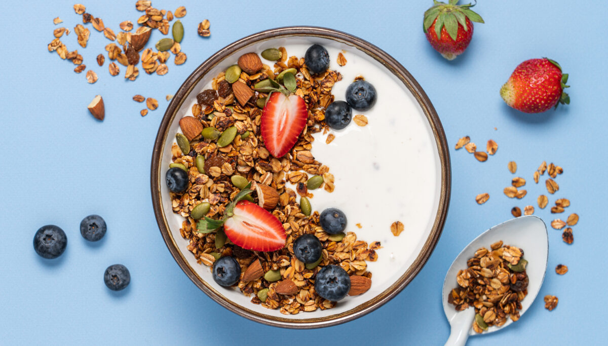 Healthy breakfast with homemade granola, berries and greek yogurt. Oatmeal, nuts, strawberries and blueberries in bowl on bright blue background.