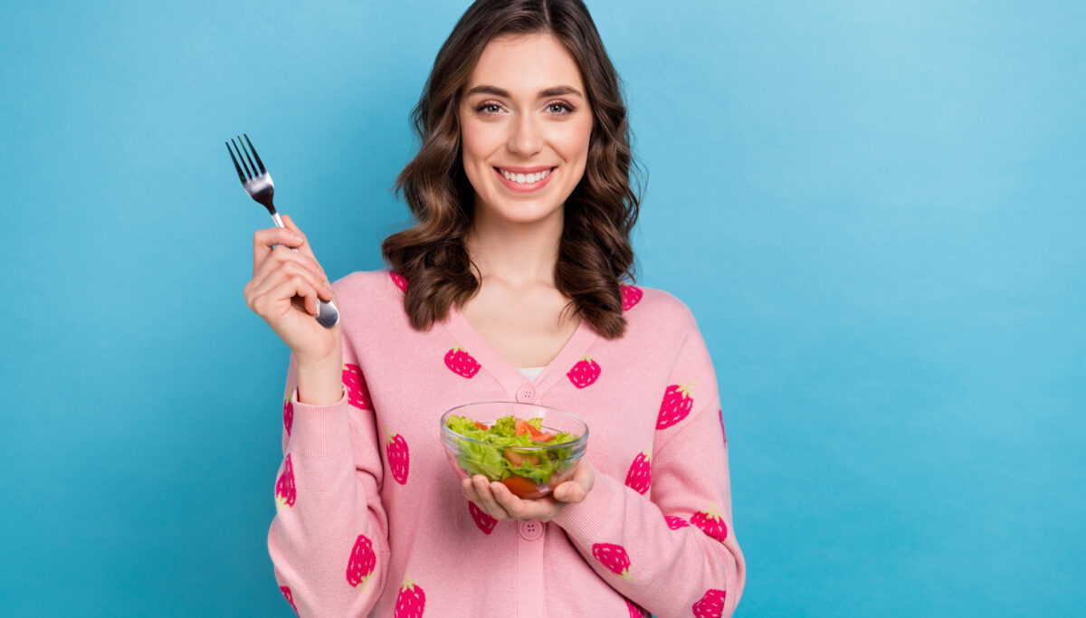 Photo of pretty lady dressed pink cardigan eating fork salad bowl emtpy space isolated blue color background.