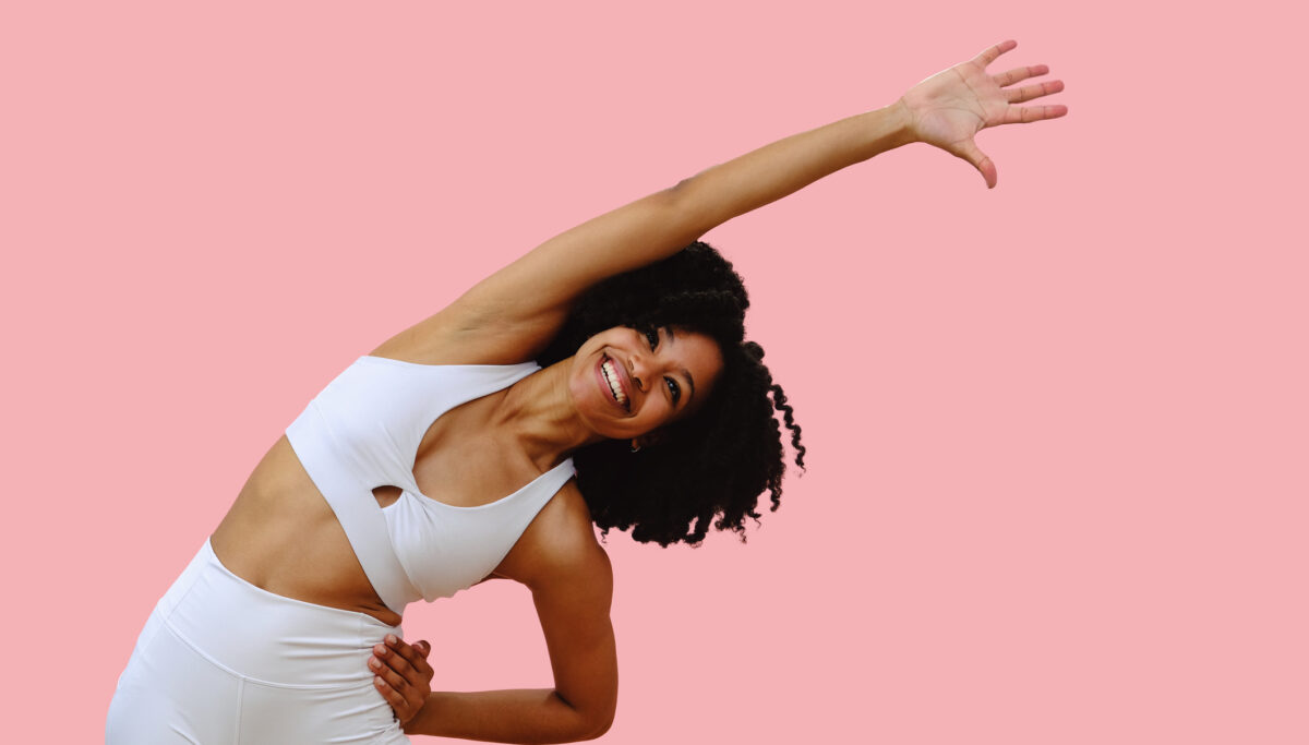 Portrait of young woman wearing sportswear stretching with arm out, against pink studio background