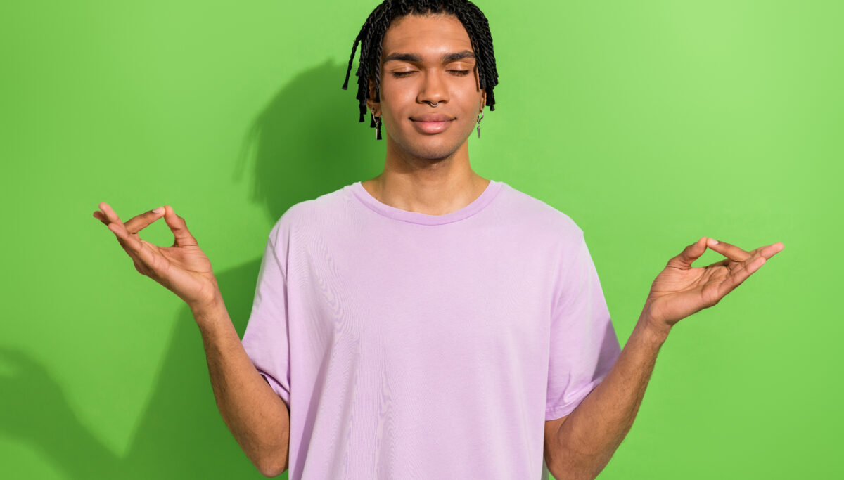 Portrait of calm focused nice young man closed eyes hands fingers meditate isolated on green color background.