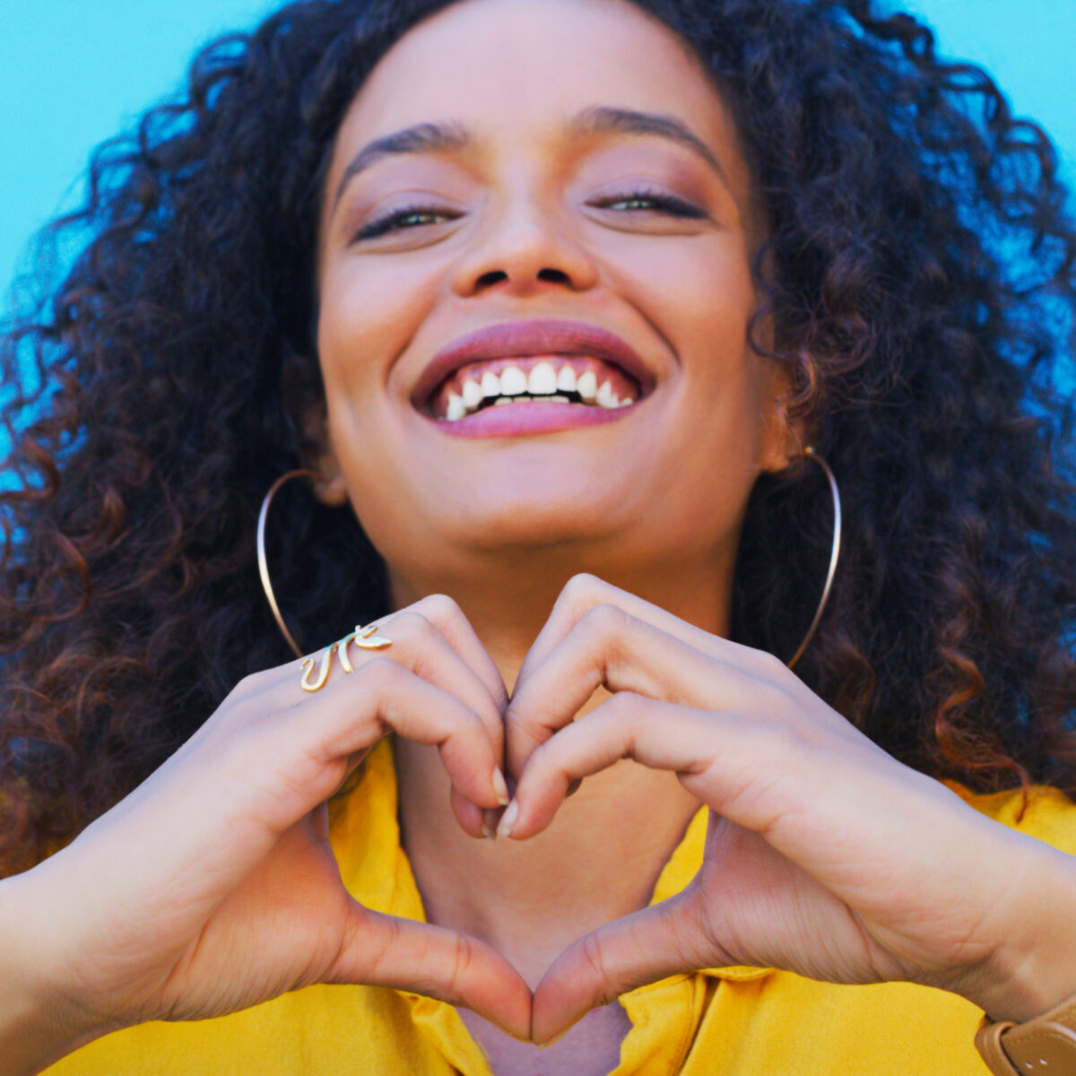 Heart, hands and portrait of woman with sign of love, care and empathy with a smile on blue, wall or studio background. Compassion, emoji and face of model with happiness in beauty or fashion