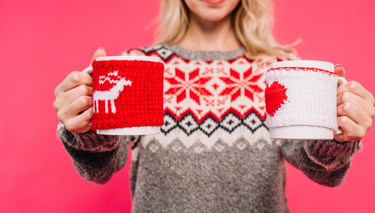 cropped image of girl in sweater holding two different cups isolated on pink