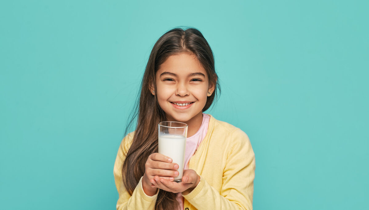 Portrait female child with a glass of milk in her hands, isolated on turquoise background. Milk is good for children's health