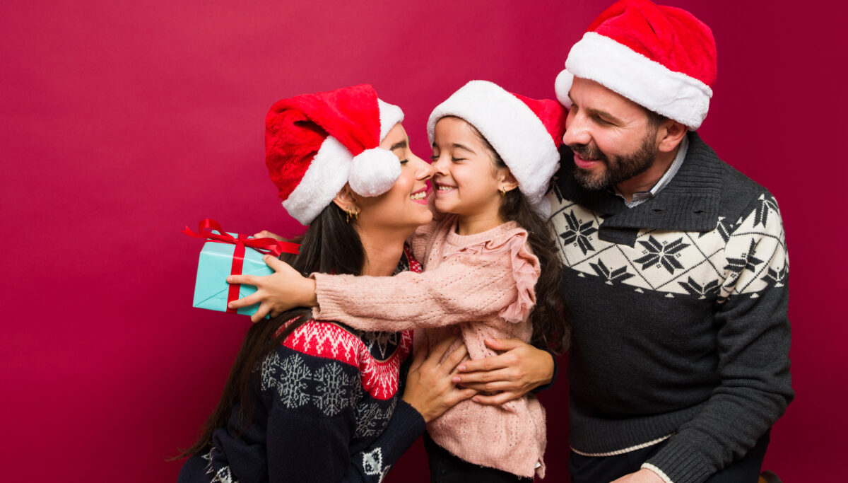 Loving family with santa hats hugging their cute daughter while opening the christmas presents