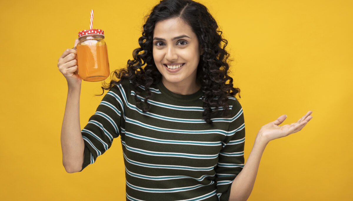Shot of a young women standing isolated over yellow background drinking non-alcoholic drink to improve drinking habits.