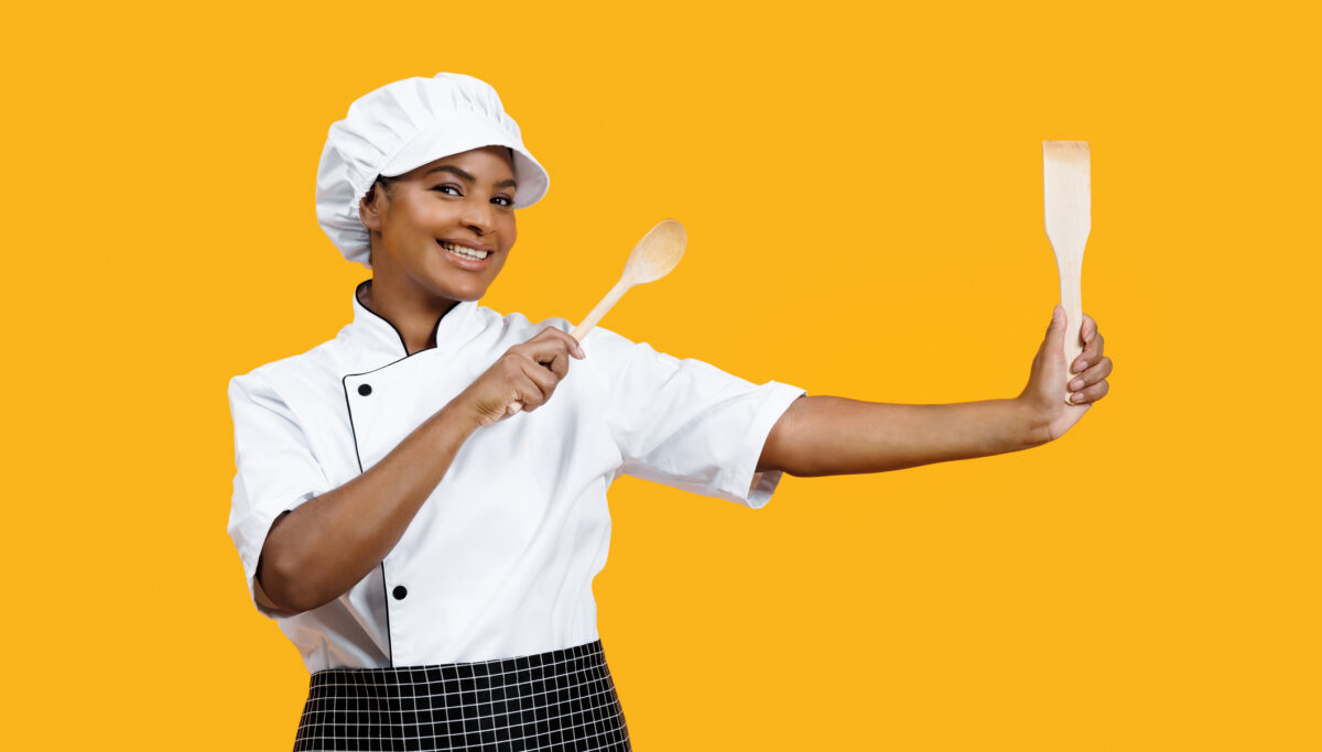Friendly female chef with radiant smile holding cooking utensils