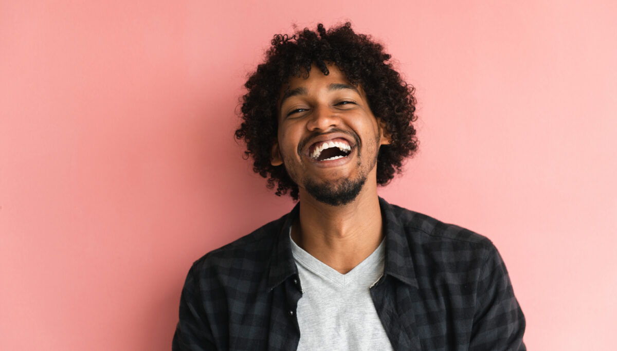 Casually dressed African-American guy posing in front of pink background.