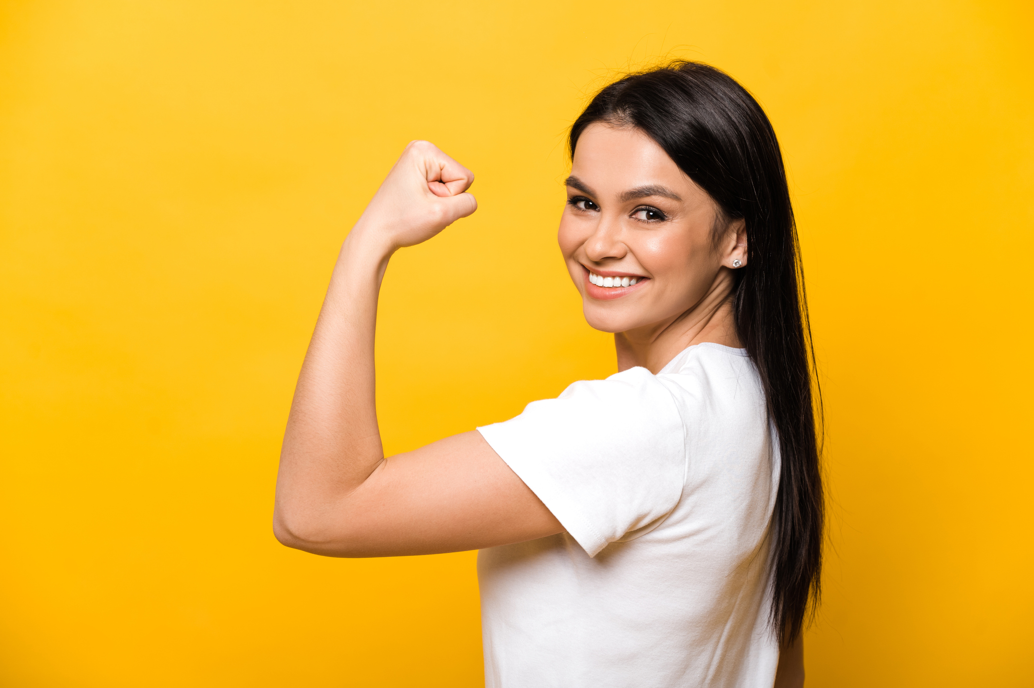 Happy and smiling woman standing showing her strength using her arm against an orange background.