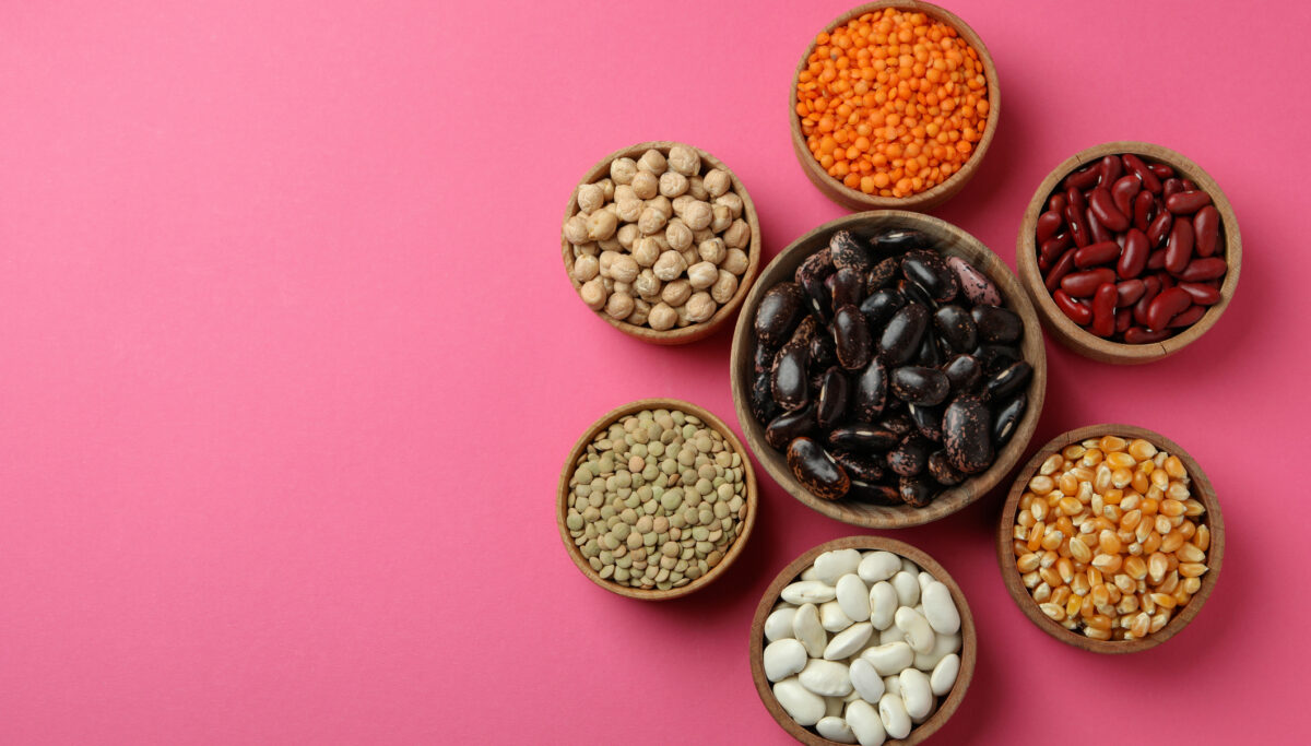 Flat lay composition with different types of beans on pink background