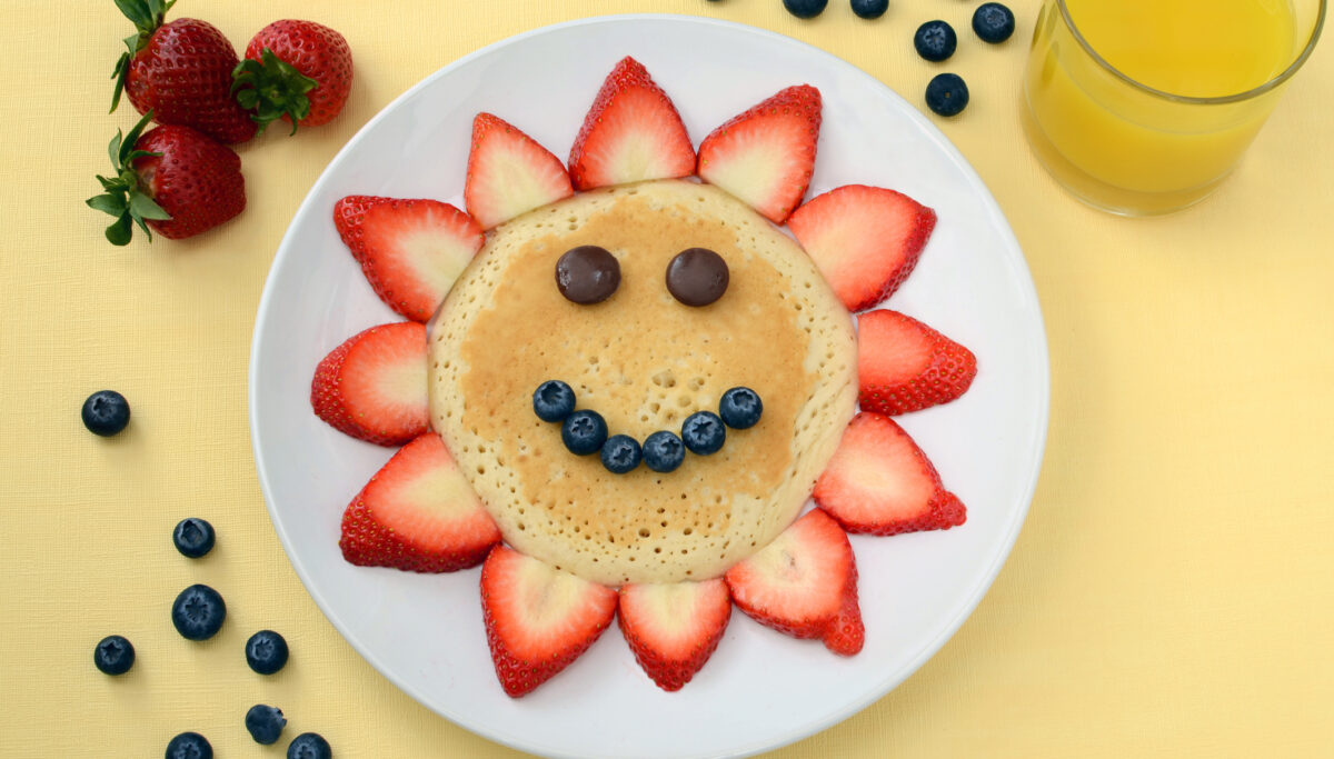 Creative children's food. Pancake with smiley face of berries. Healthy pancakes on yellow background with fruit.
