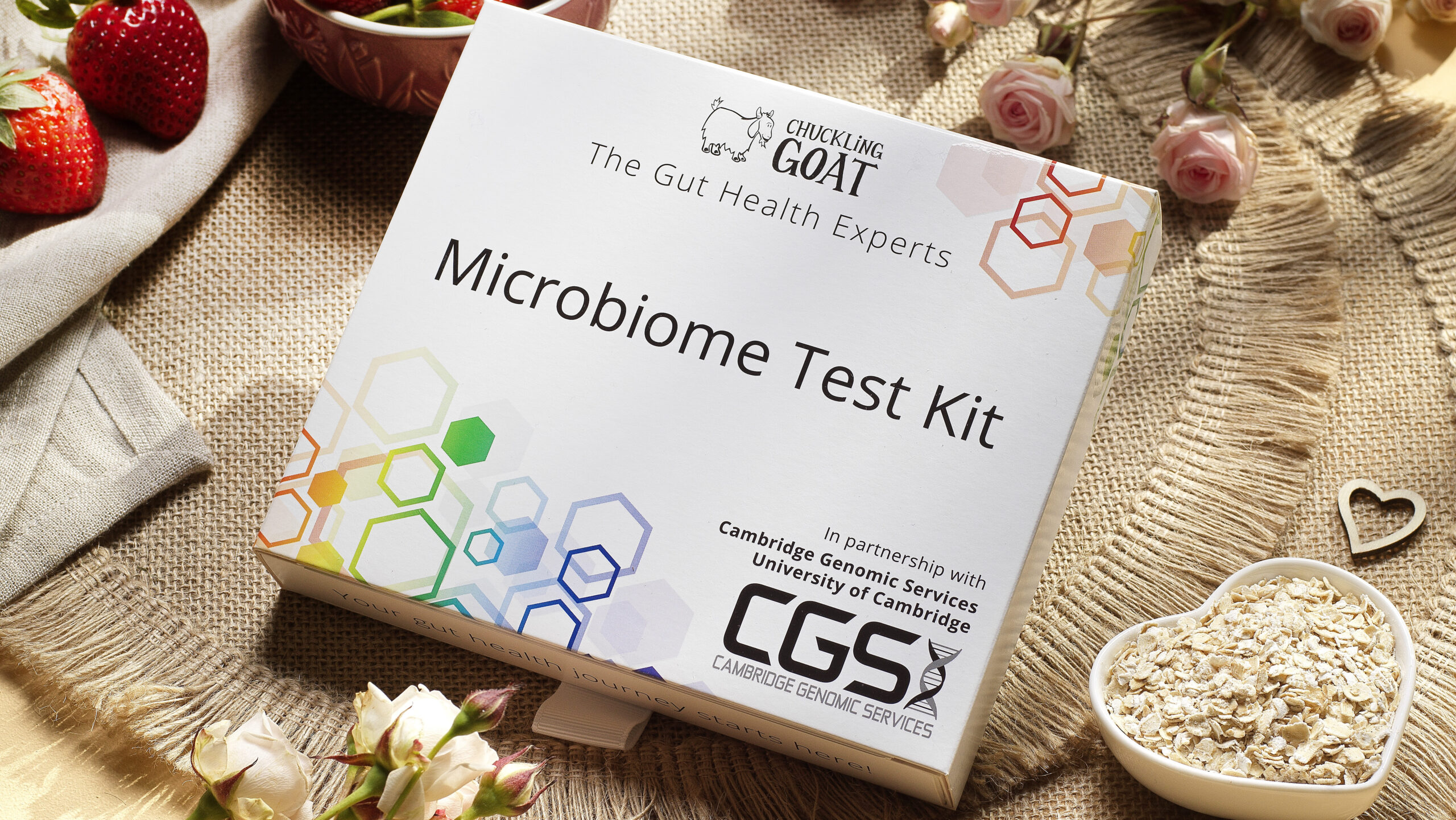 A picture of Chuckling Goat microbiome test kit box on table with nice textures, fruit, roses, and oats.