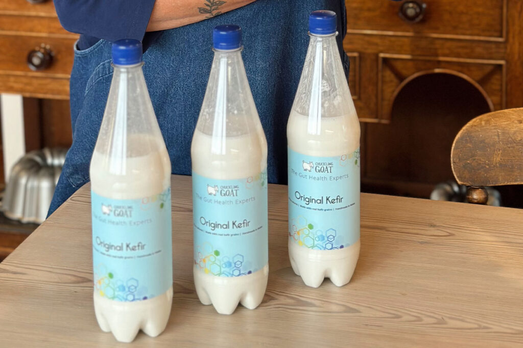 Image of 3 bottles of Chuckling Goat Original Kefir on farm kitchen table. Shann Jones in background.