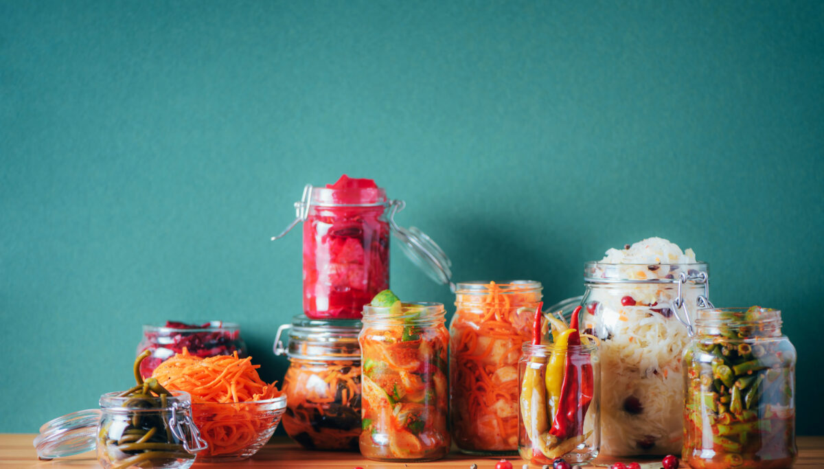 Assortment of various fermented and marinated food over wooden background, copy space. Fermented vegetables, sauerkraut, pepper, garlic, beetroot, korean carrot, cucumber kimchi in glass jars.