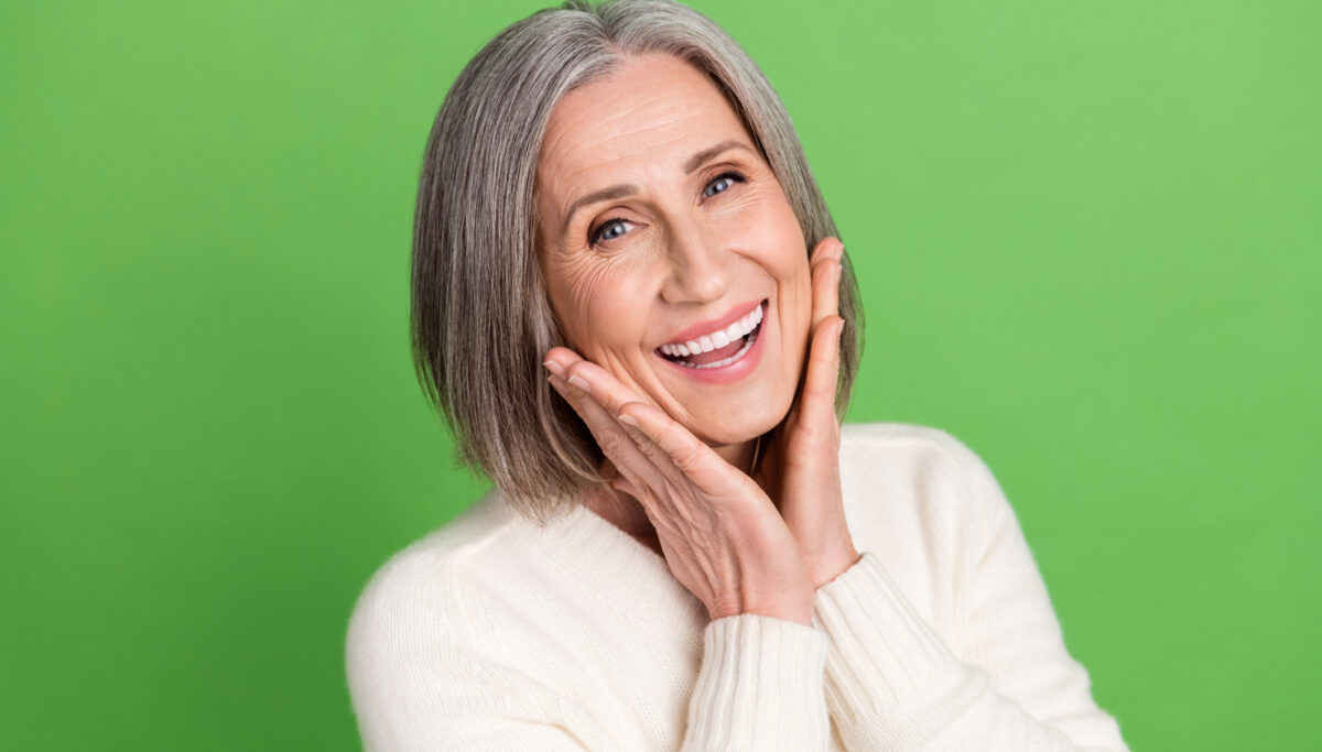 Photo of happy lady pensioner middle age hands touch cheeks laughing enjoy her new face lotion cream advert isolated on green background.