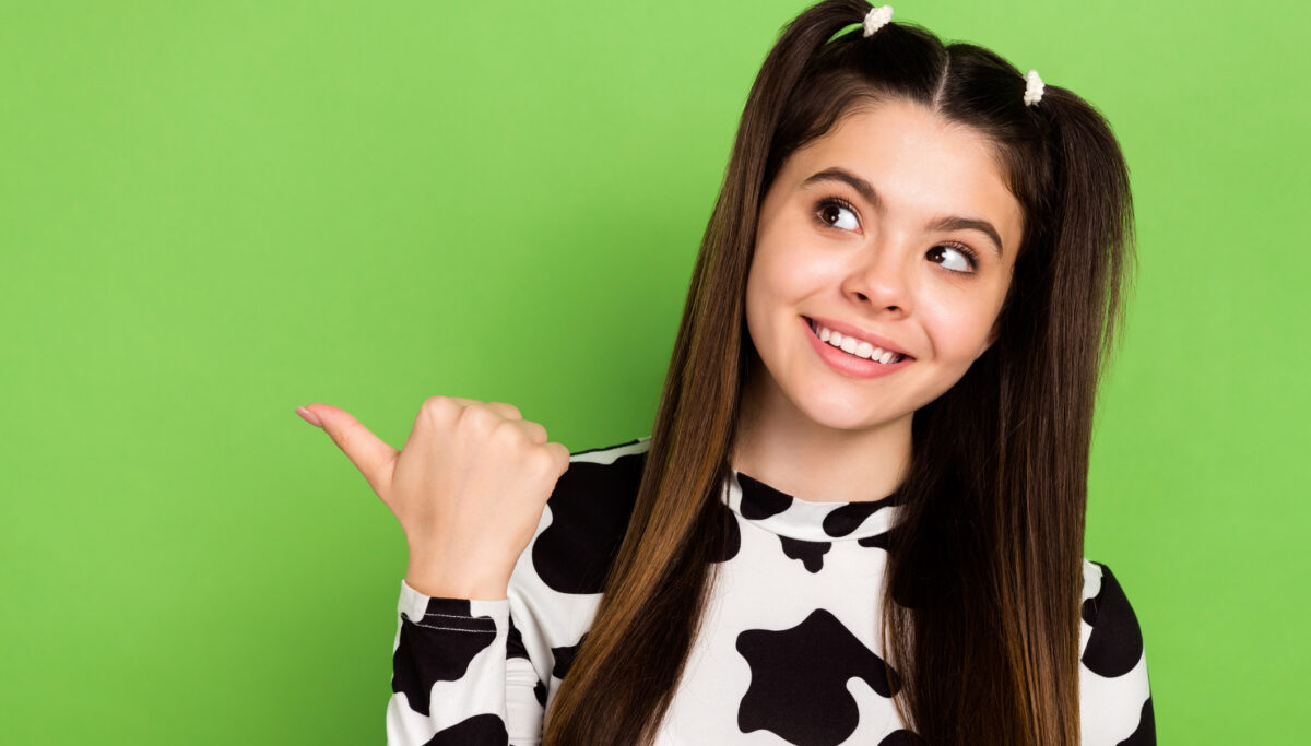 Photo of charming lovely girl beaming smile look indicate finger empty space offer isolated on green color background.