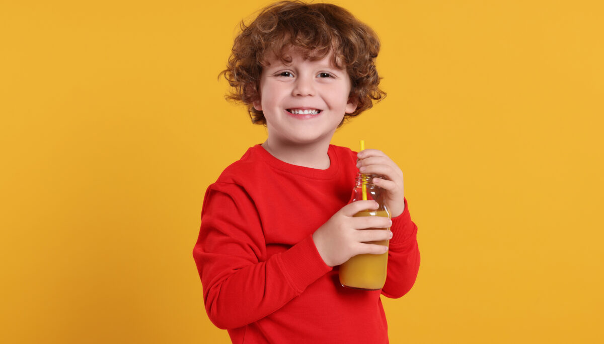 Cute little boy with glass bottle of fresh juice on orange background