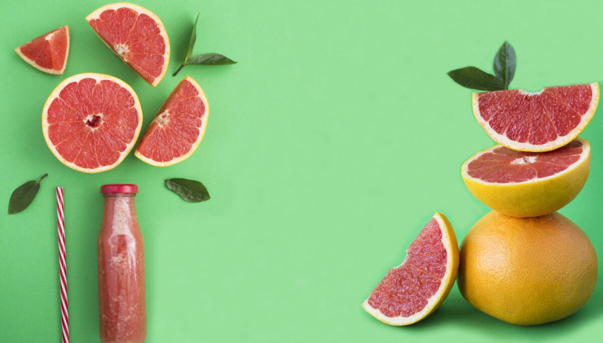 Grapefruit smoothie in a glass bottle and pyramid of grapefruit on the green background. Copy space. Close-up.