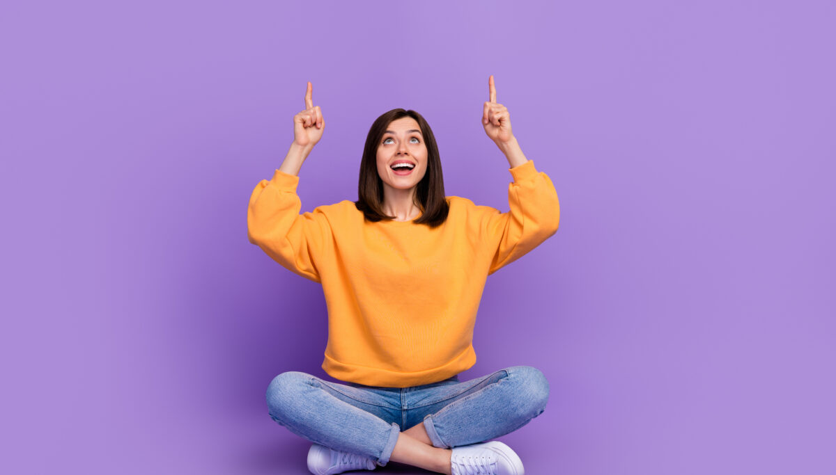 Full body size photo of charming adorable lady sitting crossed legs looking up fingers point mockup useful tips isolated on bright violet color background.