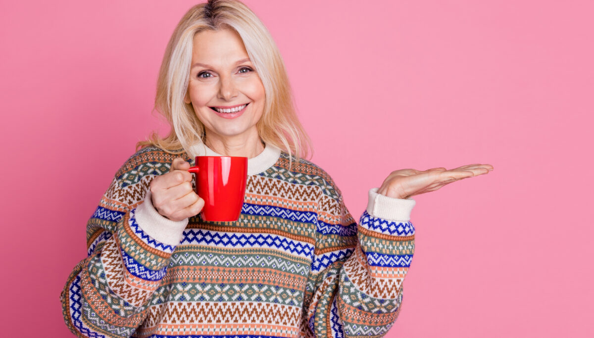 Portrait of nice aged woman hold mug empty space wear sweater isolated on pink color background.