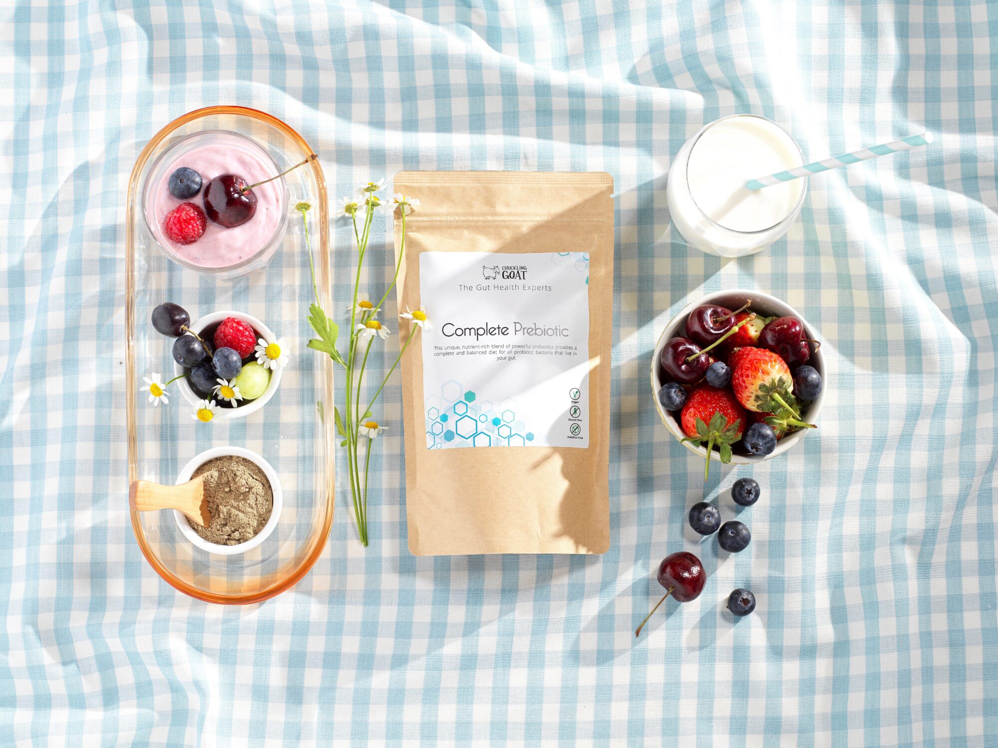 Image of Chuckling Goat Complete Prebiotic on blue and white picnic blanket among different fruits.