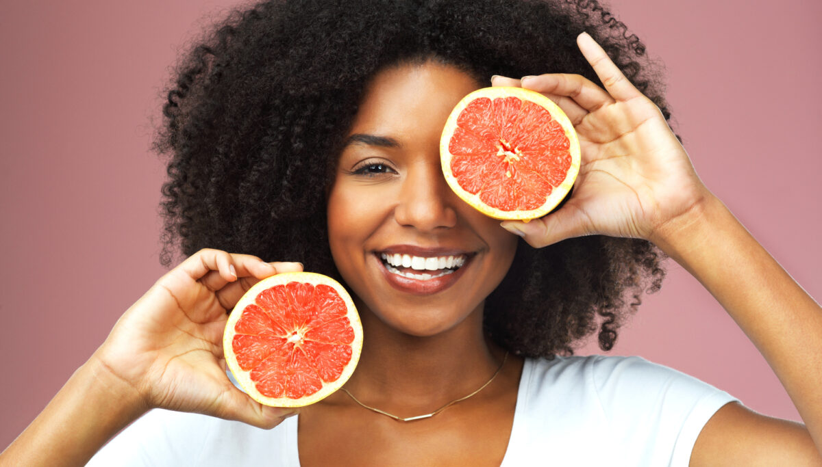 Studio shot of an attractive young woman covering her eye with slices of grapefruit against a pink background