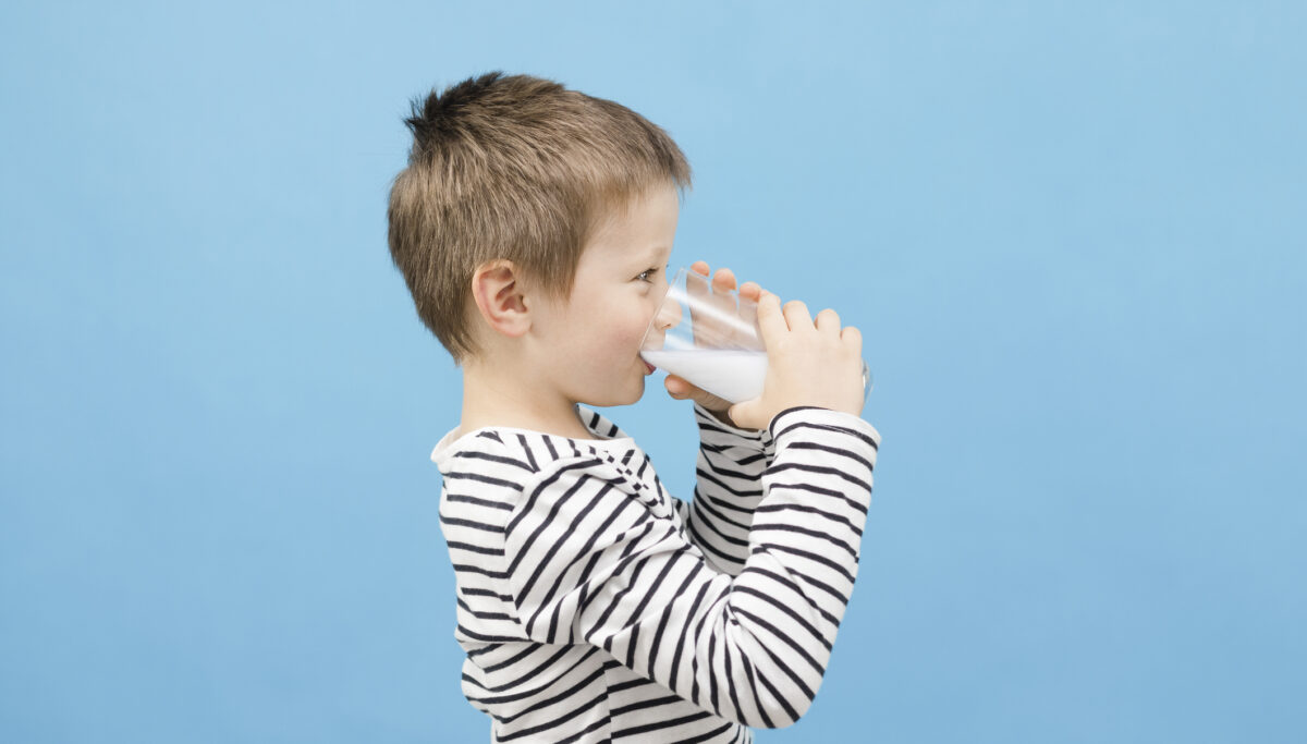 Cute caucasian boy drinks milk or kefir from a glass glass on a blue background. The benefits of milk and fermented milk products for children.