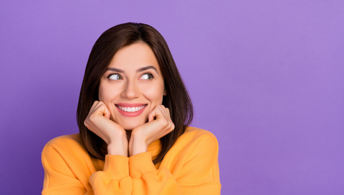 Closeup photo of young lady wear yellow shirt toothy smile touch cheeks look dreamy empty space isolated on purple color background.