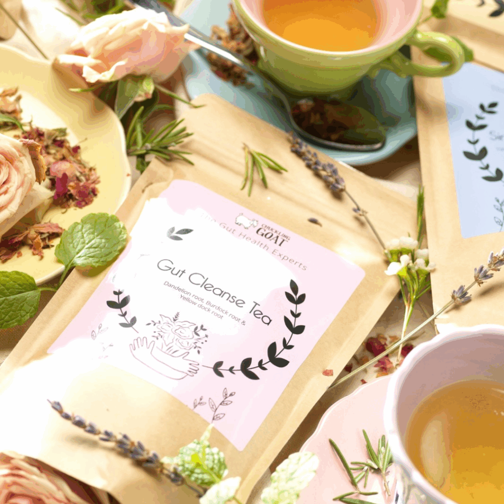 A photo of Chuckling Goats Gut Cleanse Tea, surrounded by petals and leaves, and 2 cups of tea.