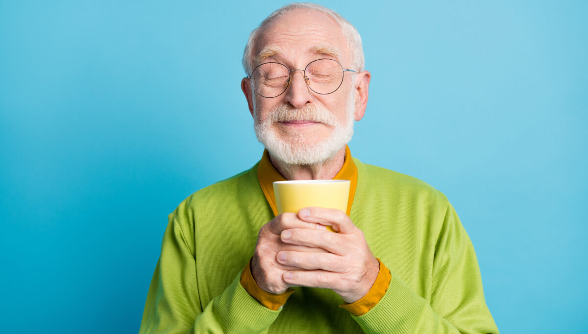 Photo of pensioner old man hold cup eyes closed sniff aroma wear eyeglasses green pullover isolated blue colour background.
