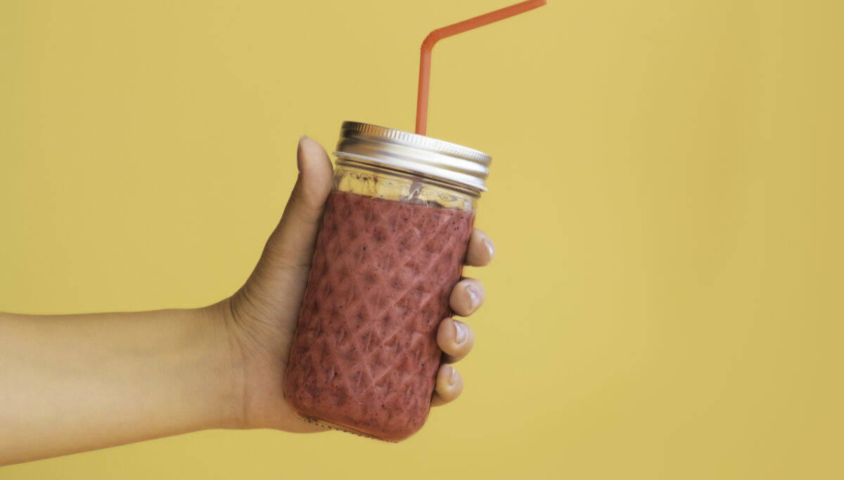 hand holds a jar of smoothies on a monochrome yellow background. High quality photo