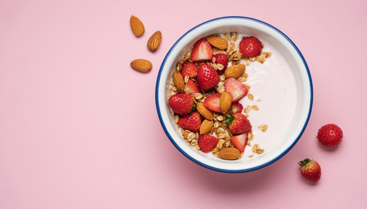 Yogurt with fresh berries, homemade granola, in bowl. Healthy breakfast on pink background