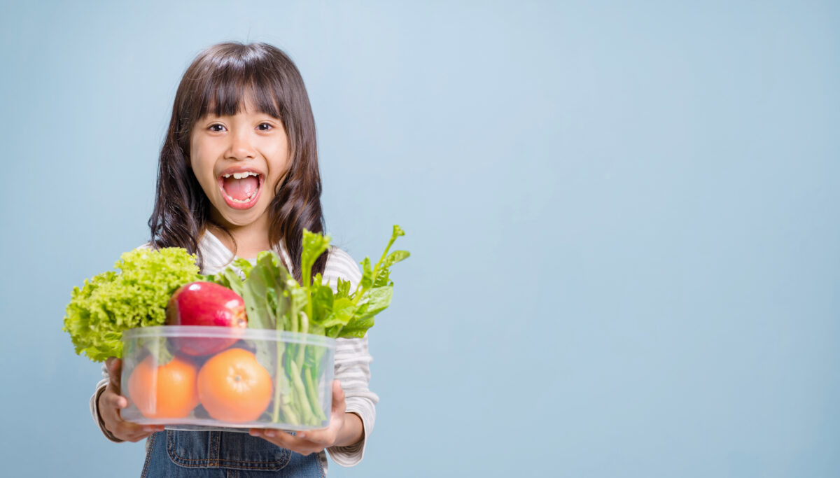 A little girl is holding a bowl with mixed vegetables and fruits.