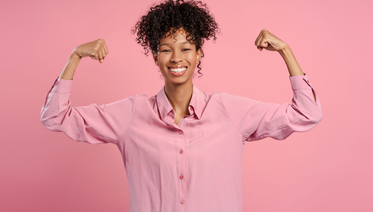 Portrait of excited woman showing biceps rejoicing isolated on pink background looking at camera. Concept of victory, competition