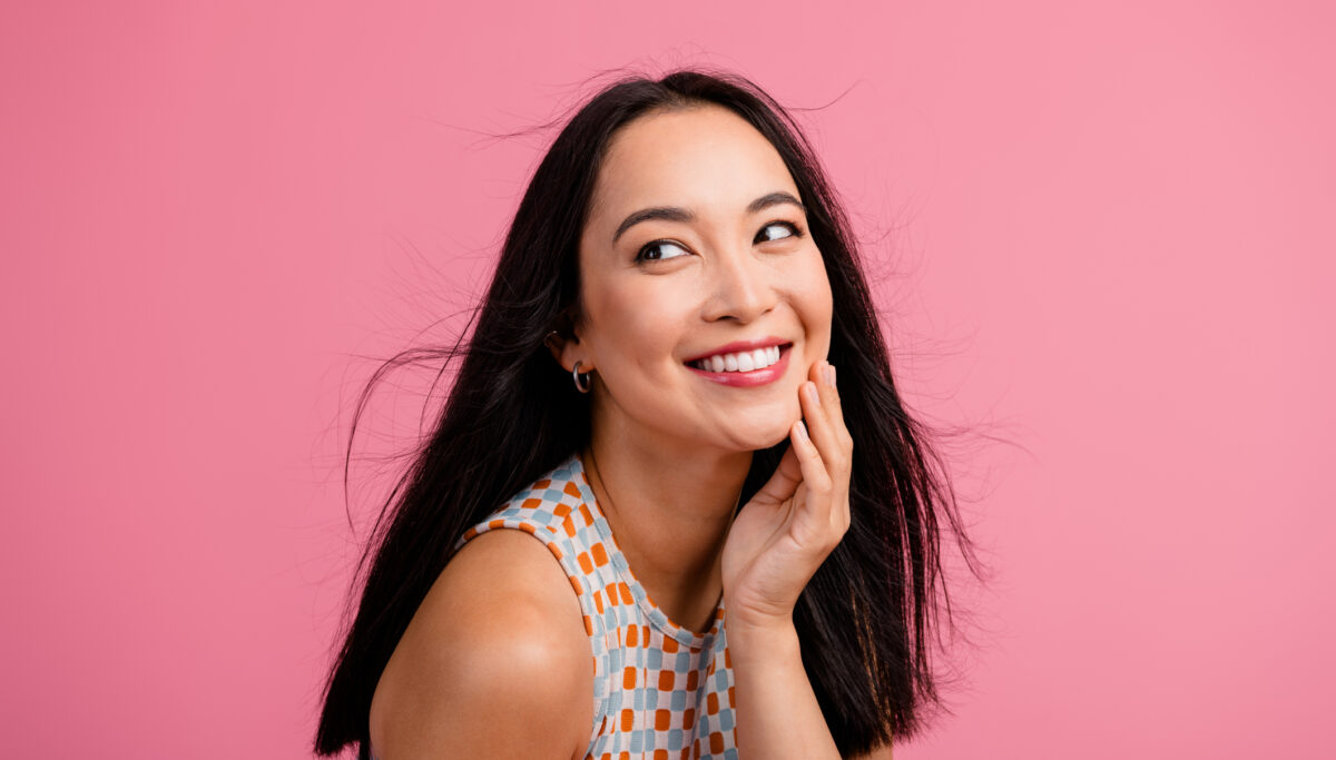 A woman with a joyful smile, posed in front of a pink backdrop.