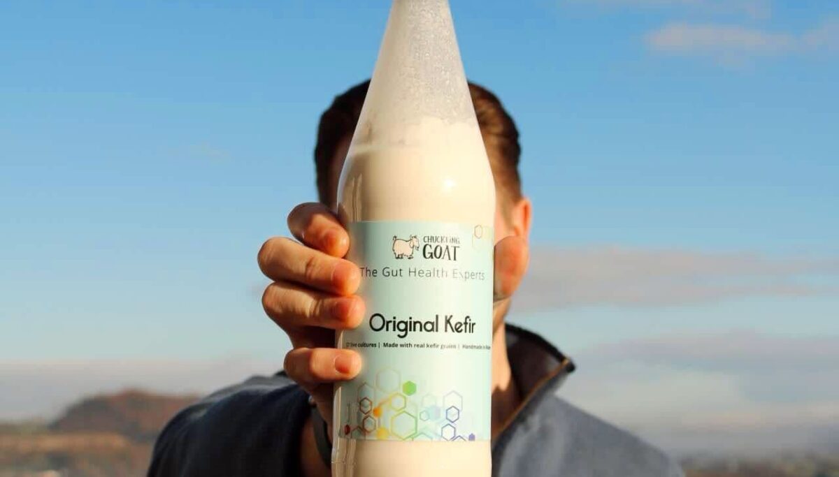 Image of man holding Chuckling Goat Kefir bottle in front of beautiful landscape