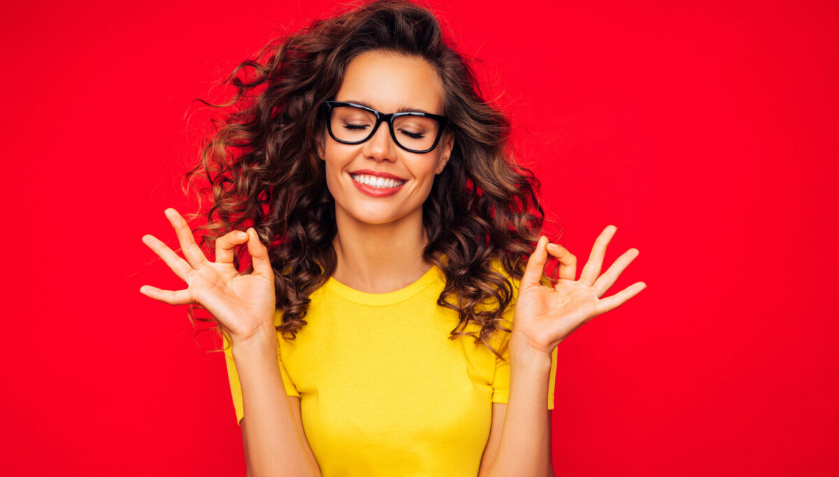 Smiling woman, showing OK sign using hands, on a red background.