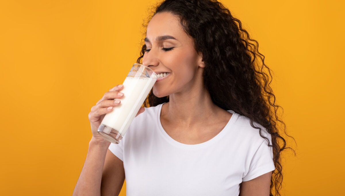 Woman drinking a glass of milk on a yellow coloured background.