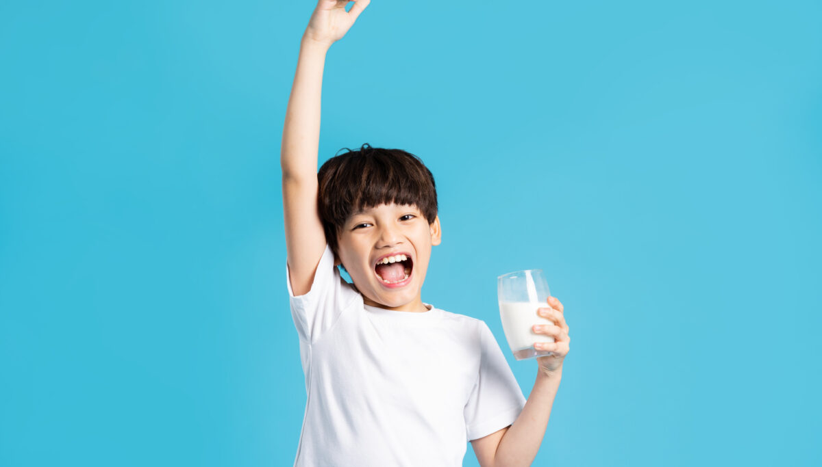 Photo of boy holding a glass of milk, on a blue background.