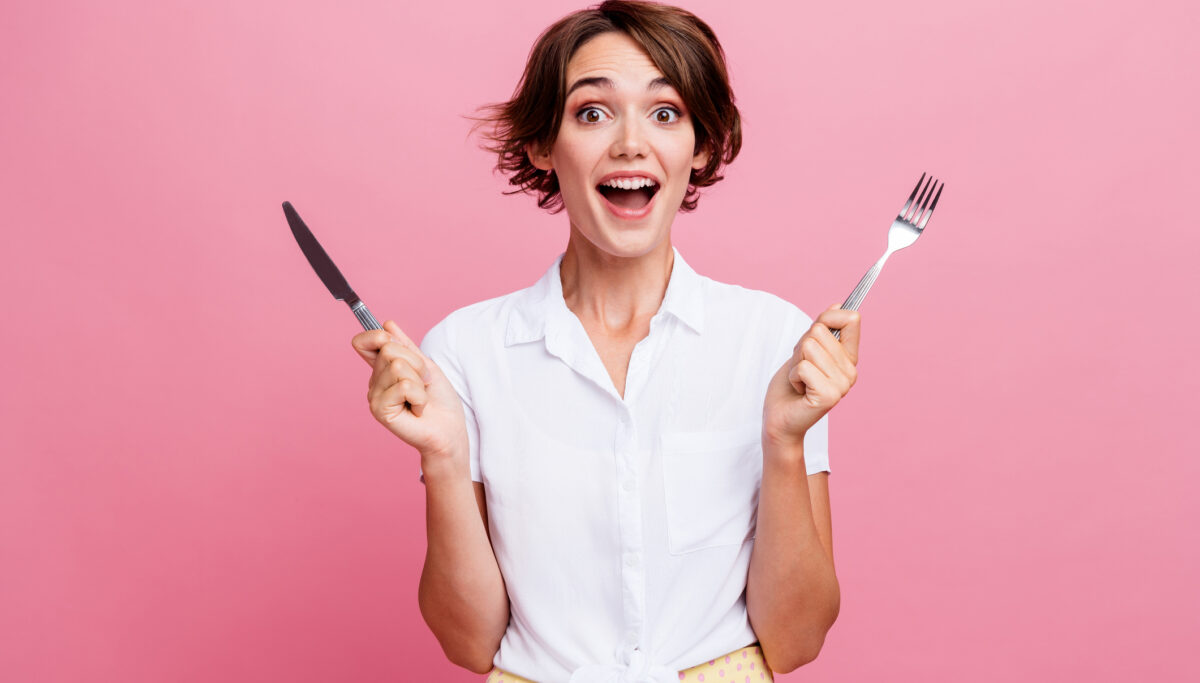A photo of a woman holding a knife and fork, with a happy face on a pink coloured background.