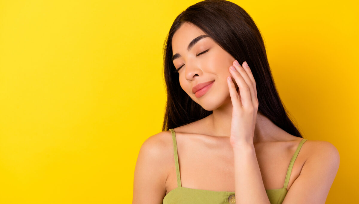 Photo of adorable charming young girl dressed clothes smiling arm cheek empty space isolated yellow color background.