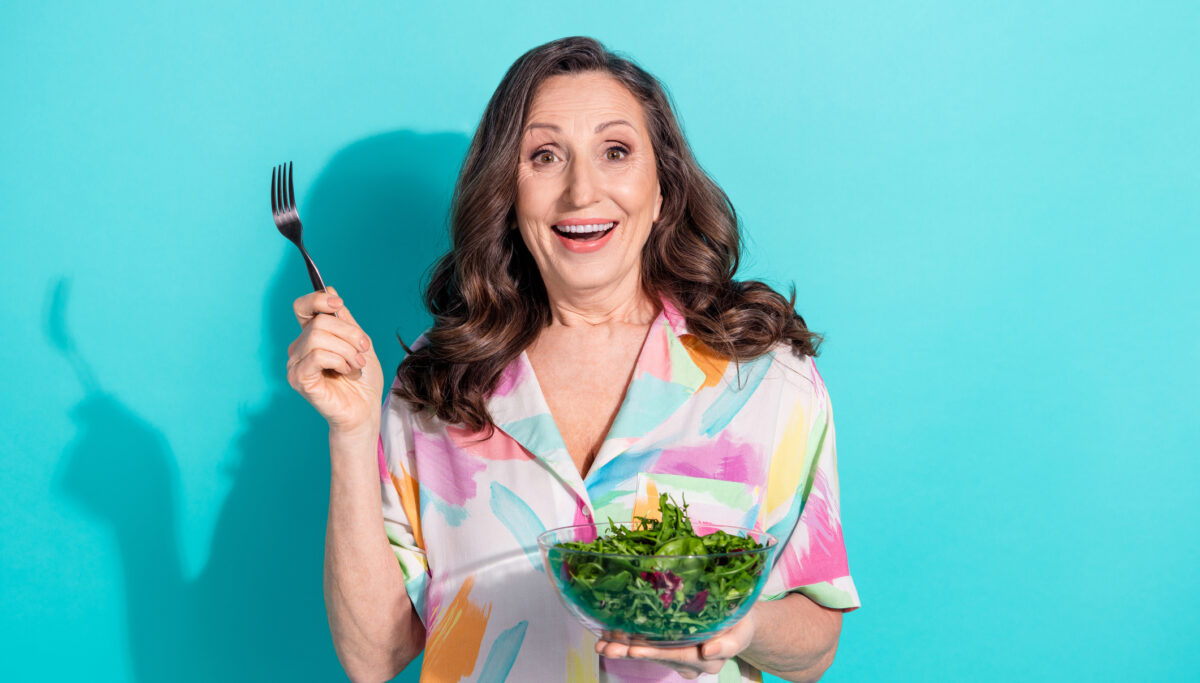 Photo of female eating a salad excited wearing colourful outfit isolated on blue background.