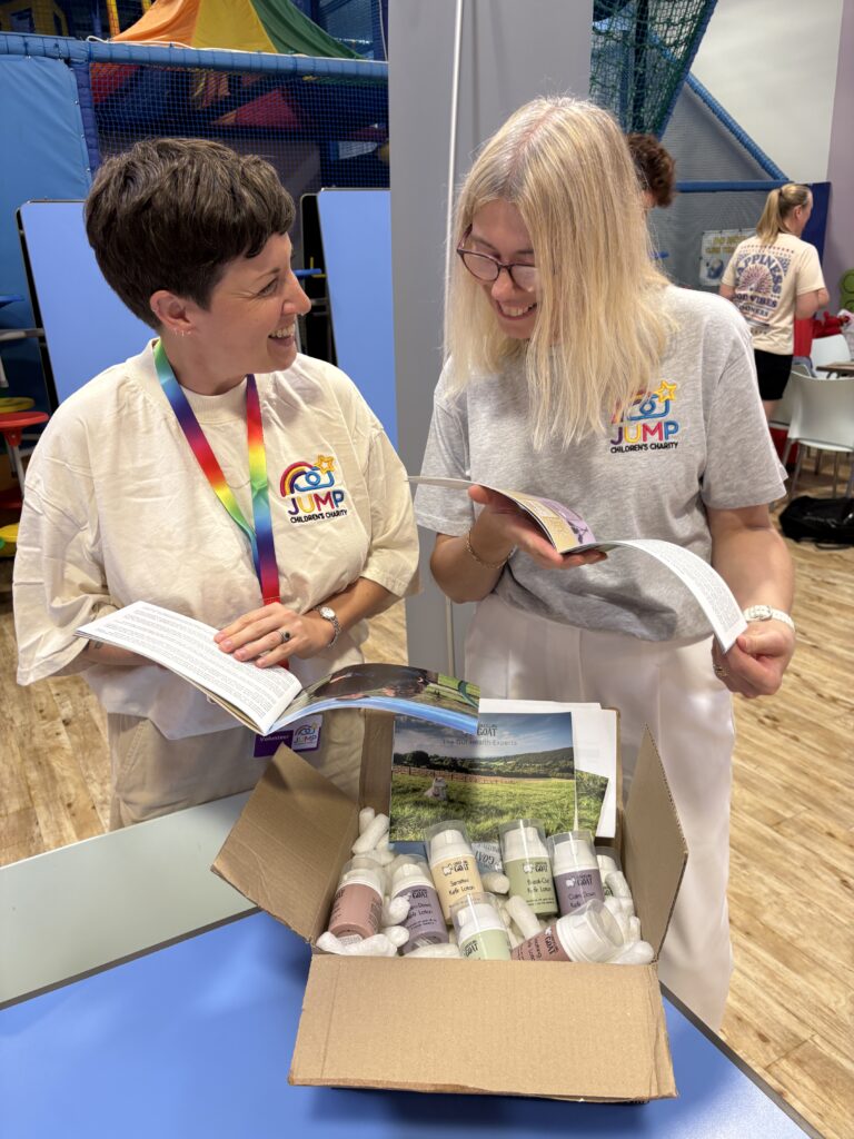 Image of two women working JUMP charity t-shirts opening a box of Chuckling Goat goodies.
