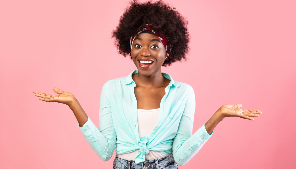 Cheerful Woman Shrugging Shoulders Smiling To Camera Posing Standing Over Pink Studio Background. Young Millennial Female Holding Two Invisible Objects On Hands