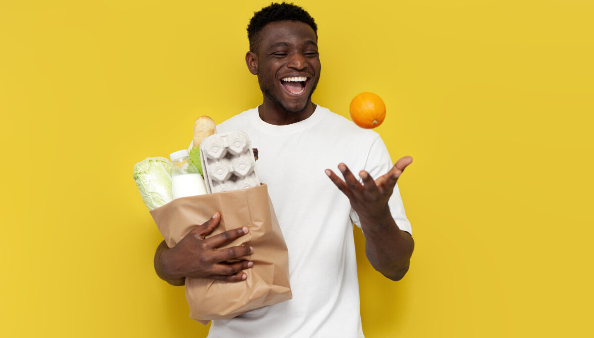 happy african american male shopper holding eco bag with groceries and nodding orange against yellow isolated background, guy customer rejoicing and smiling