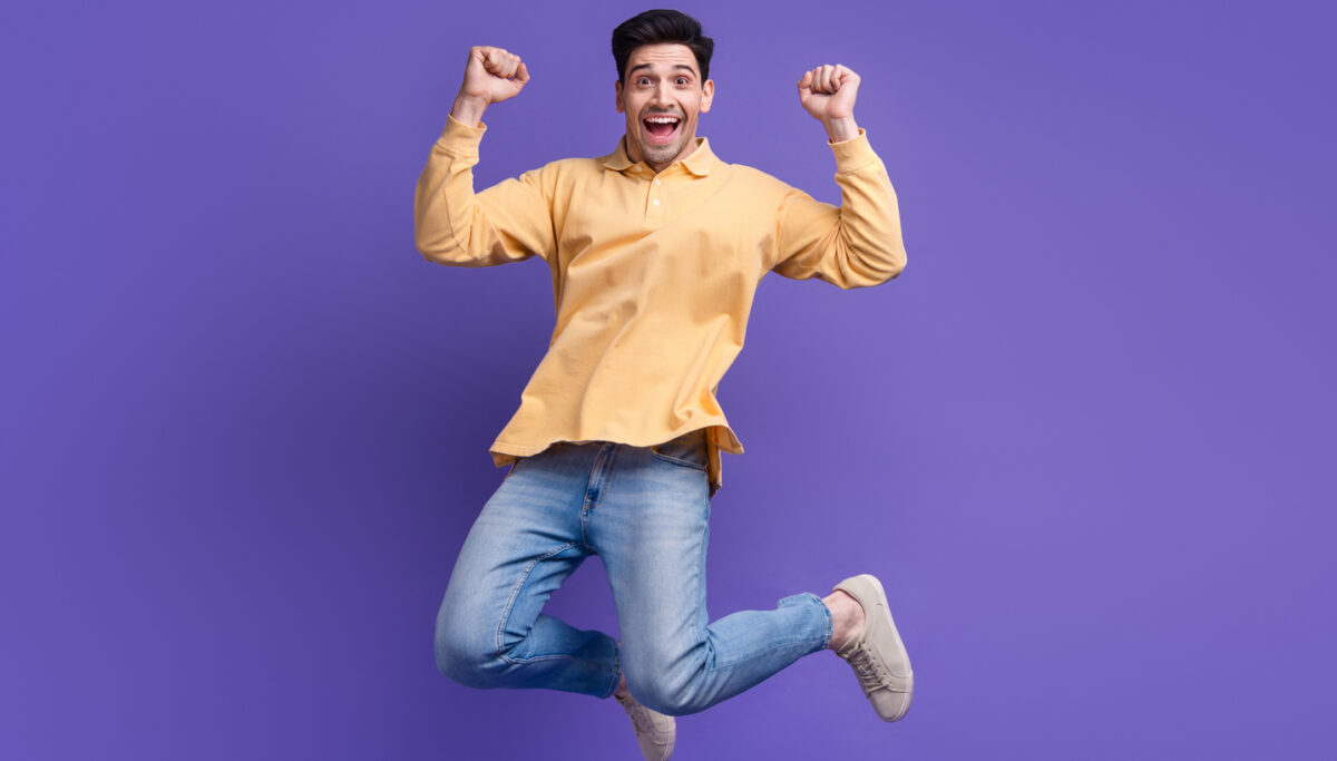 Full size photo of attractive young man jumping raise fists celebration dressed stylish yellow clothes isolated on purple color background.