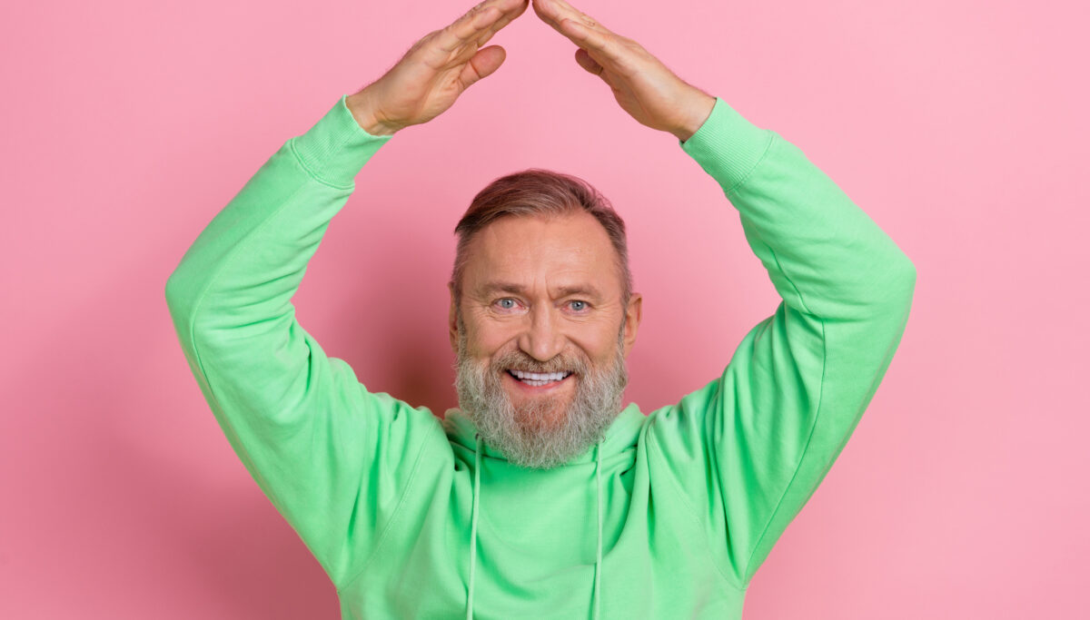 Photo of cheerful funky man wear green sweatshirt showing arms roof isolated pink color background.
